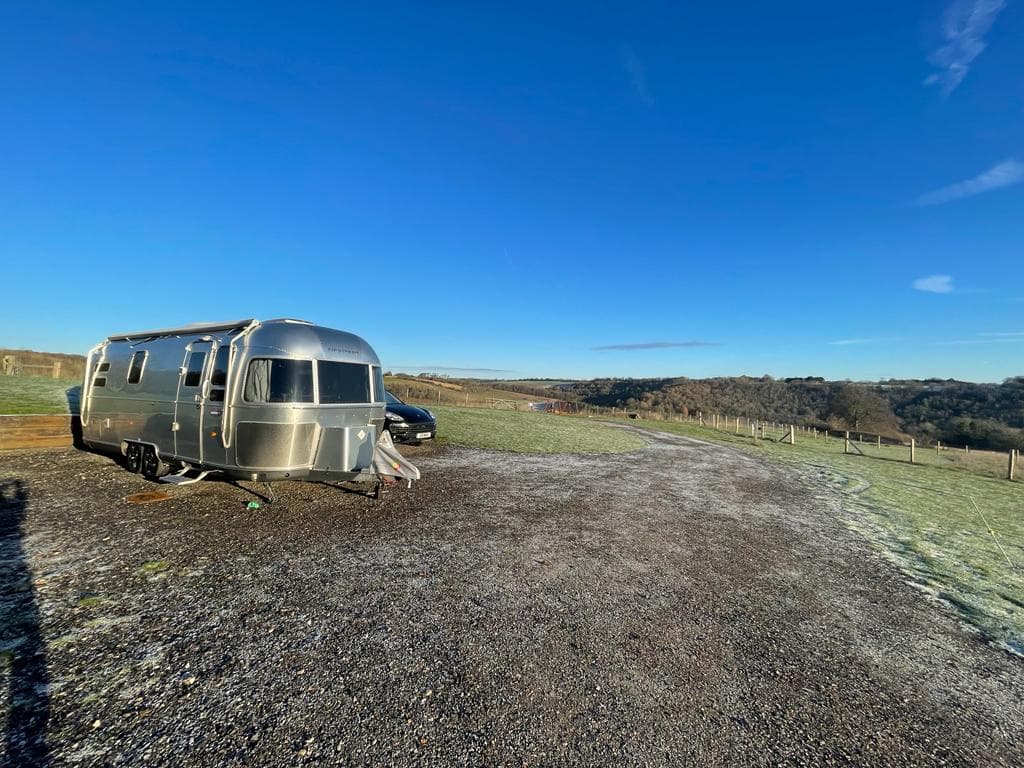 An Airstream caravan on a frosty gravel pitch at Cholsey Grange under a clear winter sky, with the valley beyond.