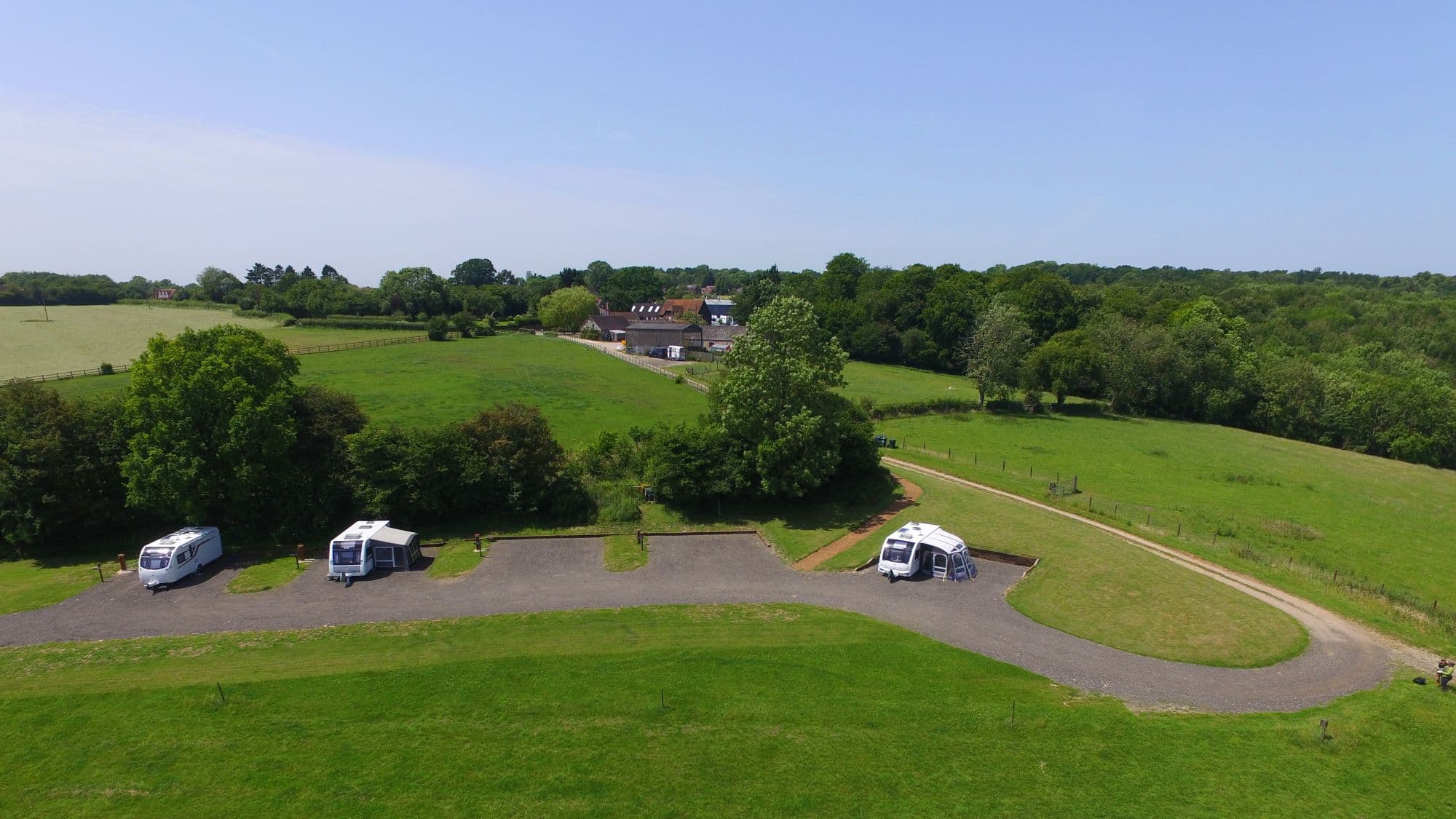 Caravans with awnings on the gravel hardstanding pitches at Cholsey Grange, seen from the air, with the farm buildings beyond.