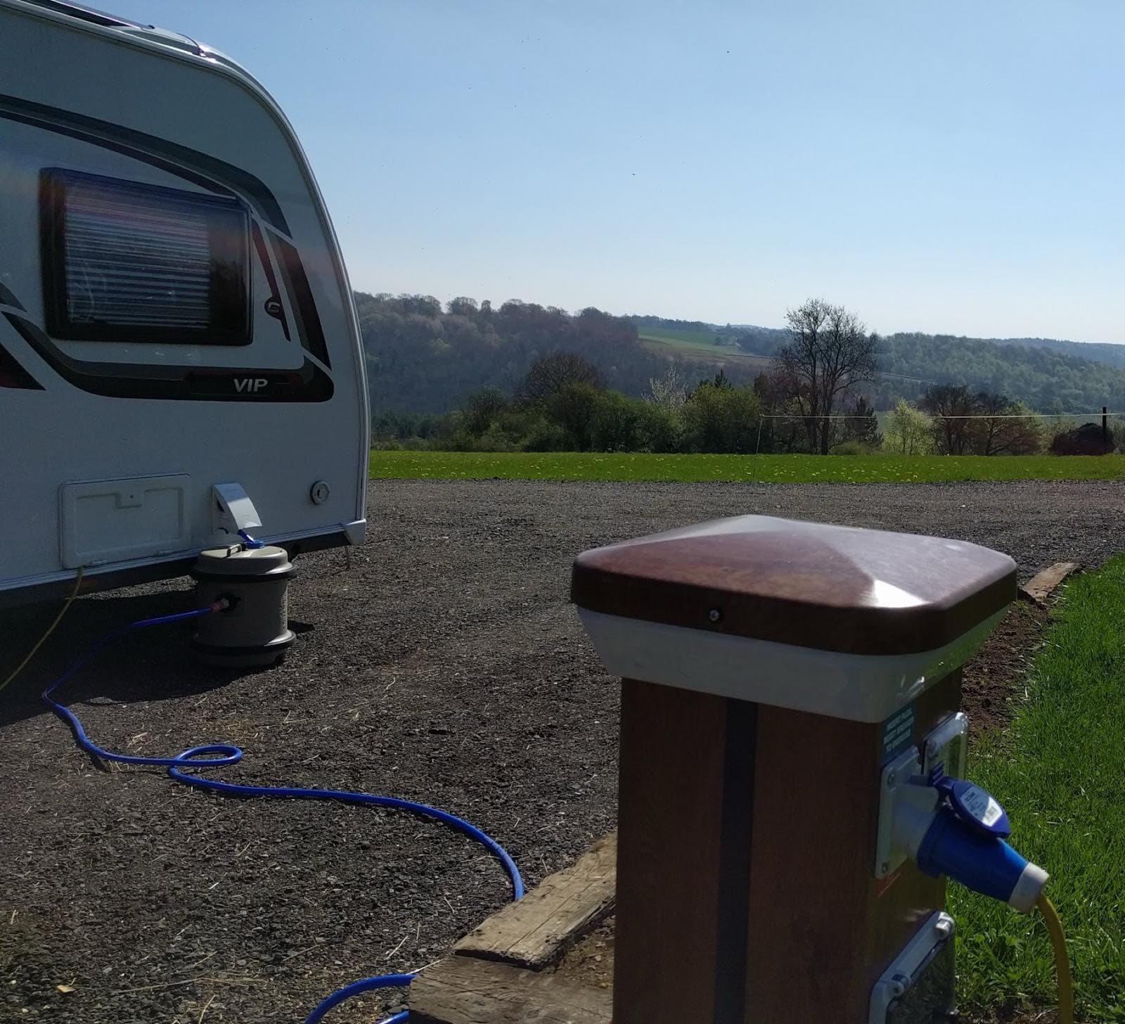 A service bollard beside a hardstanding pitch, providing electric hook-up, fresh water and grey waste.