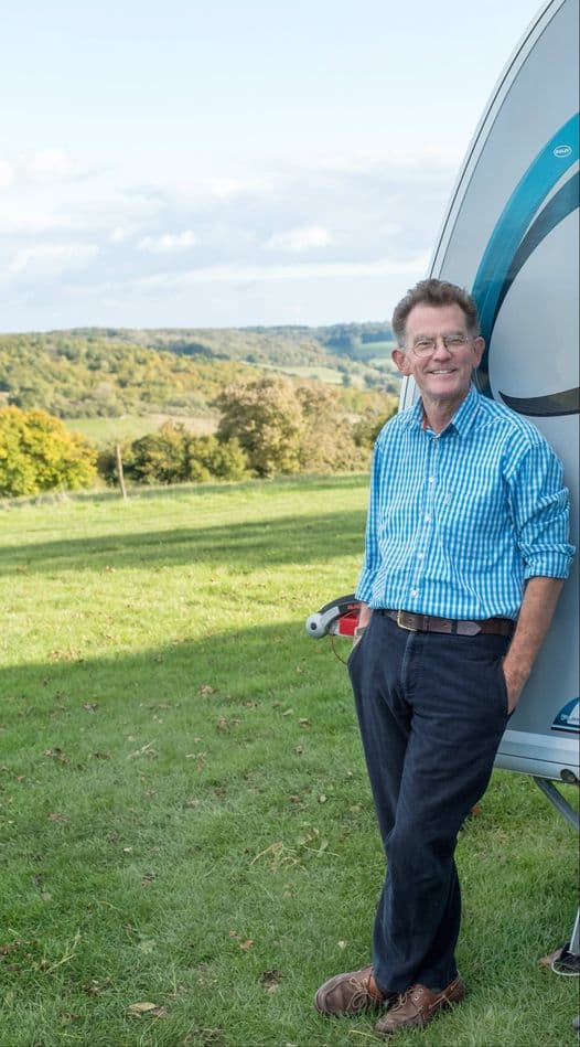 Ted Howard-Jones leaning against a caravan on the CL field, with the wooded Hambleden Valley behind him in autumn.