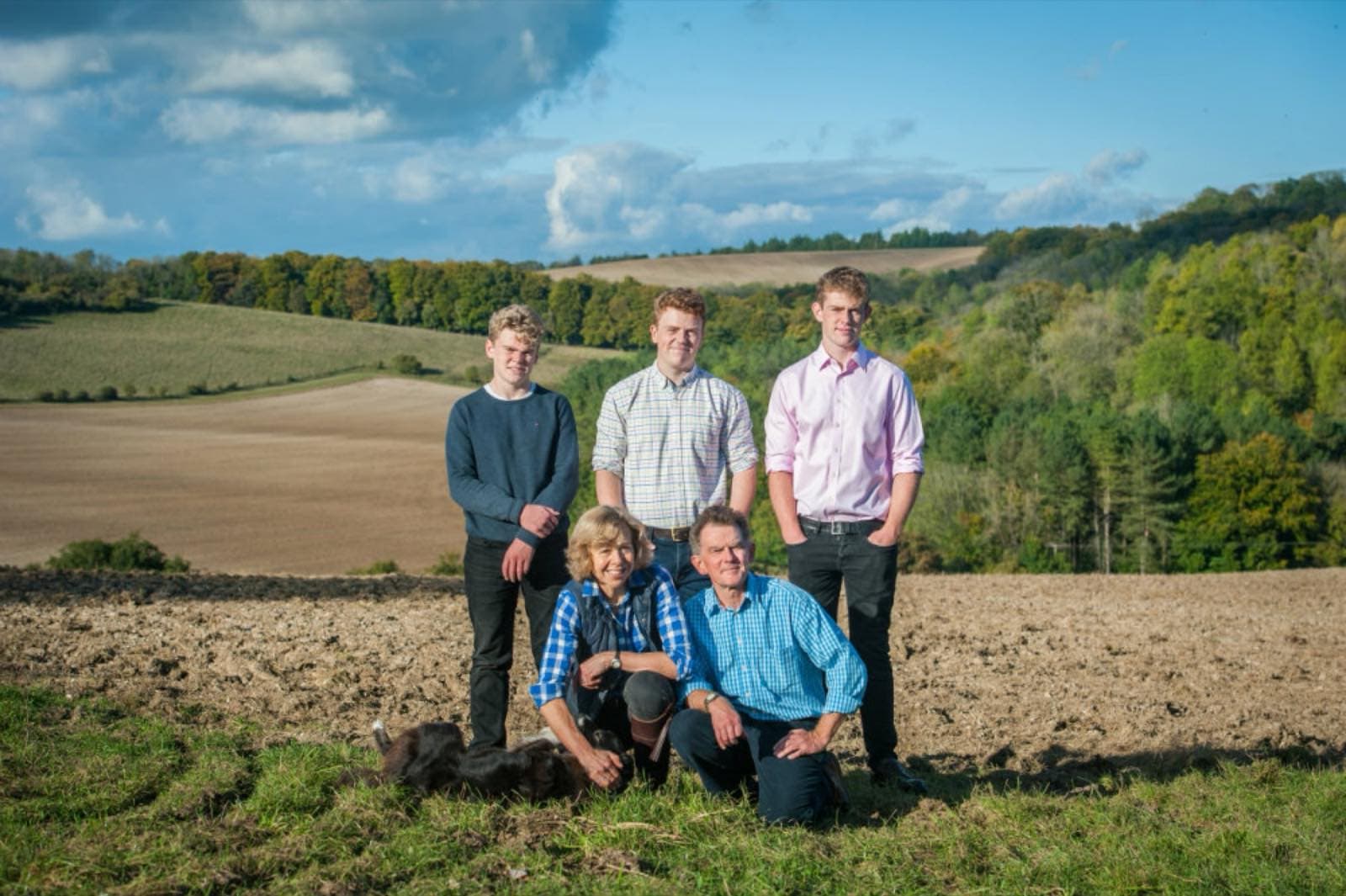 The Howard-Jones family standing in a ploughed field on the farm, with woodland behind.
