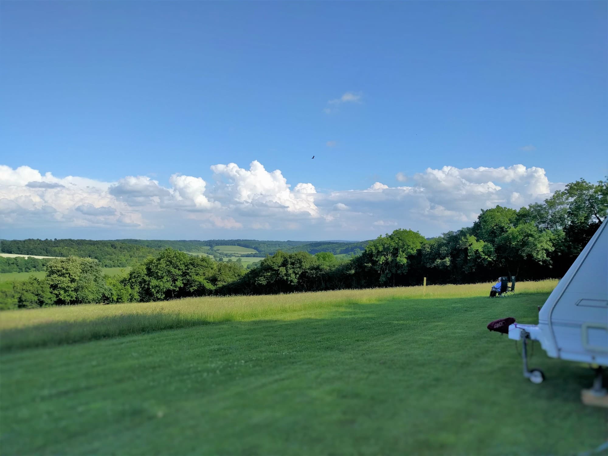 Guests relaxing on the grass at Cholsey Grange, looking out over the wooded Hambleden Valley under summer clouds.